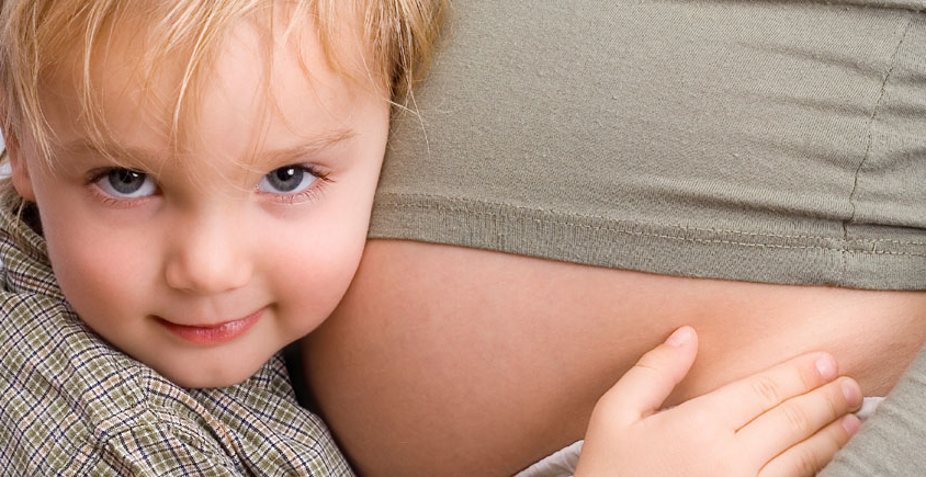 A child is hugging the belly of a pregnant woman