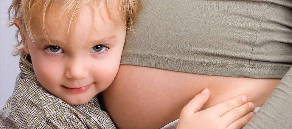 A child is hugging the belly of a pregnant woman