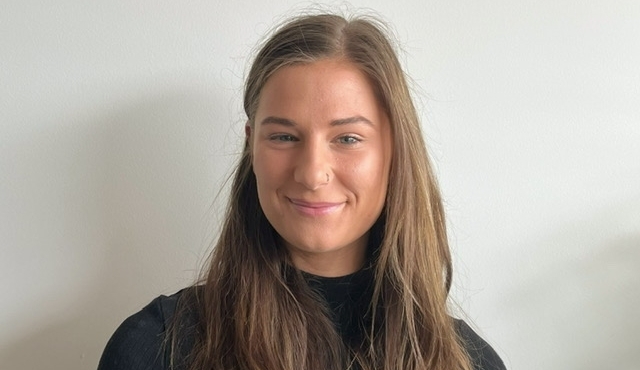 A woman with long hair smiling in front of a wall