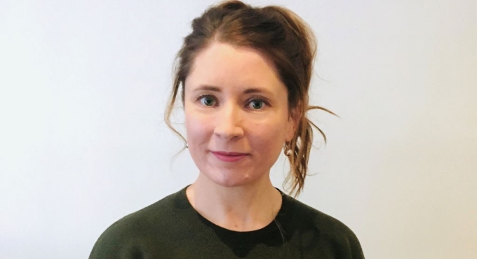 A woman in a green shirt is standing in front of a white wall.