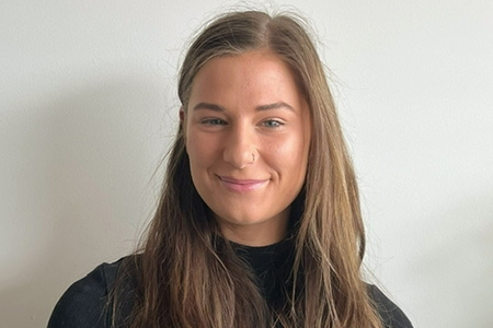 A woman with long hair smiling in front of a wall