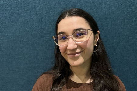 A woman in glasses smiling in front of a blue wall